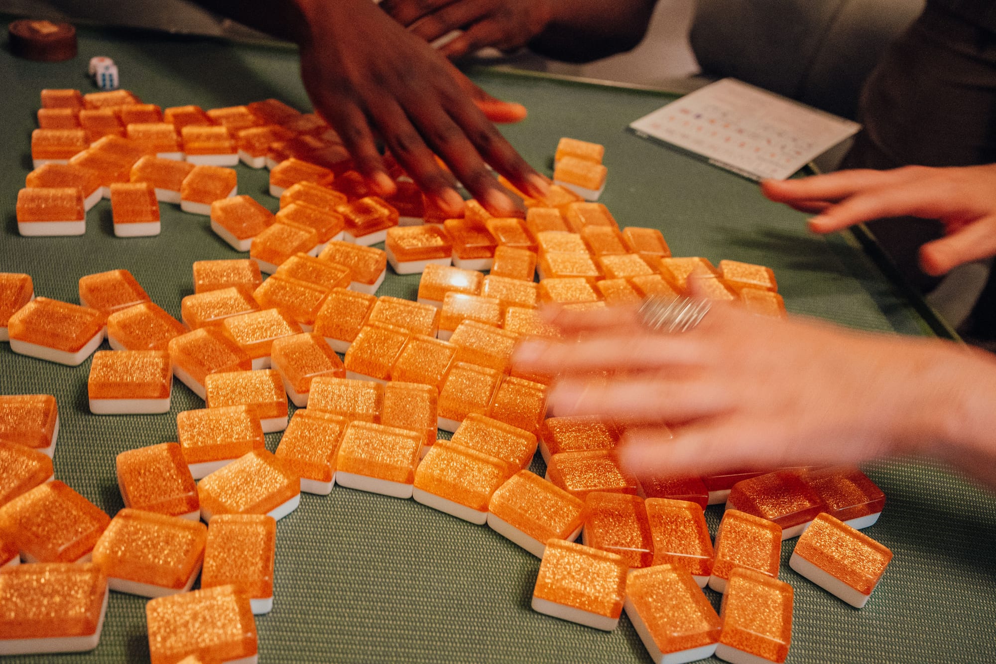 Hands shuffling mahjong tiles across green felt